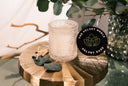 Velvet Ease Candle on a golden pedestal with Eucalyptus leaves and matches.
