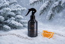 A black spray bottle labeled 'VELVET home' stands in snow with pine branches and orange slices around it, against a snowy winter background.