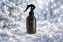 A black trigger spray bottle labeled 'VELVET home' stands in the snow against a sparkling, bokeh winter background with pine branches.