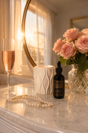 Glass of pink champagne, bouquet of roses, bottle of Velvet Drops, and pearl necklace on a marble surface.