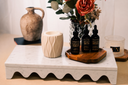 Three bottles of 'Velvet Drops' and a white warmer on a wooden tray with decorative items including a vase and flowers.