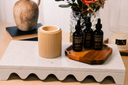 Three bottles of 'Velvet Drops' and a tan warmer on a wooden tray with decorative items including a vase and flowers.