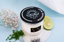 Candle labeled 'Morning Mist' with a black lid, surrounded by flowers and citrus on a light blue background.