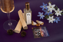 A styled flat-lay featuring a bottle of Golden Twilight Mini Air & Linen Mist with a gold cap, surrounded by a glass of sparkling wine, wooden rollers, pinecones, raw amber, blue and white flowers, and a tarot card on a deep purple background.