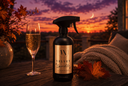 A dark spray bottle labeled 'VELVET Sparkle' stands on a wooden table beside a filled champagne flute, with autumn leaves, a knitted blanket, and an outdoor sunset sky in the background.