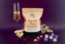 A stand-up pouch of Velvet Powder by The Velvet Noble, styled on a dark purple background with a champagne flute, cream-colored tablets, pine cones, and small white and blue flowers.