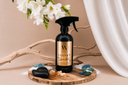 A bottle of Velvet Sparkle Multipurpose Spray on a wooden tray with sea glass, sand, amber and florals on a beige background.