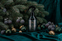 A dark pump bottle labeled 'VN Velvet Home' is styled on deep teal velvet fabric with pine branches, purple berries, and gold and green ornaments.