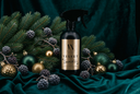 A black trigger spray bottle with a gold label reading 'VN VELVET sparkle' is styled on draped dark teal fabric with pine branches, berries, and gold and green ornaments.