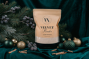 A stand-up pouch of Velvet Powder Luxury Freshener centered on a dark green velvet fabric, surrounded by pine branches, frosted berries, gold and green ornaments, and cinnamon sticks.