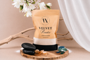 A bag of Velvet Powder carpet and upholstery powder on a wooden tray with sea glass, sand, amber and florals on a beige background.