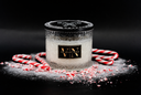 A frosted glass jar candle with a black lid and a gold 'VN' label, styled with candy canes, white powder, and crushed red candy cane pieces on a black background.