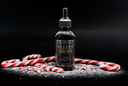 A bottle of Velvet Drops Luxury Warmer Oil by The Velvet Noble, styled with candy canes and crushed candy on a dark surface against a black background.