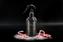 A black spray bottle labeled 'VELVET home' stands on a black surface with white salt-like powder and red-and-white candy canes around its base, against a dark studio background.