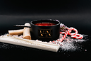 A black scented candle jar with a gold 'VN' logo, styled with white sugar, wooden wicks, and candy canes on a black background.