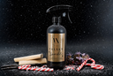 A black trigger spray bottle labeled 'Velvet Sparkle' stands on a dark surface with candy canes, vanilla beans, and dried botanicals around it against a snowy black backdrop.
