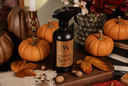 A black spray bottle labeled 'Velvet Sparkle' stands on a wooden board surrounded by pumpkins, autumn leaves, acorns, and a candle holder in a styled fall setting.