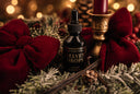 A small black dropper bottle labeled 'The Velvet Noble Velvet Drops' is styled in a festive holiday setting with red velvet bows, green frosted foliage, cinnamon sticks, pinecones, and a gold candle holder with a red candle.