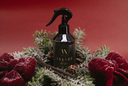 A black trigger spray bottle labeled 'Velvet home' in gold lettering, styled in a festive wreath with green frosted pine branches, red velvet bows, and cinnamon sticks against a solid red background.