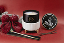 A holiday-themed candle set from VN Candles, featuring an open black and white candle jar on small wooden legs, its lid labeled 'SILENT NIGHT' shown beside it, along with vanilla beans, a decorative red bow, and a candlestick on a red background.