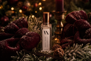 A clear rectangular perfume bottle with a metallic gold cap and a white label reading 'Silent Night', styled on green pine branches with dark burgundy bows, a candle, and warm bokeh lights in the background.