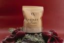 A stand-up pouch of Velvet Powder luxury freshener by The Velvet Noble, styled with red velvet bows, pine branches, and a pinecone on a dark red background.