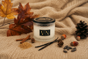 A 2-wick Vanilla Harvest candle on a woven blanket with autumn decor around it such as Vanilla beans, Cinnamon, Brown Sugar, Pinecones, acorns, and autumn leaves.