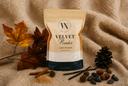 A stand-up pouch of Velvet Powder luxury carpet powder is styled on a beige textured fabric background with autumn leaves, pinecones, cinnamon sticks, and acorns. The pouch is cream and beige with a dark base and a circular 'VN' logo at the top.