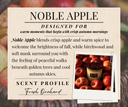 A scent profile card for Noble Apple, a scented candle. The card features a textured beige background with black text describing the scent as a blend of crisp apple, warm spice, birchwood, and soft musk, with a 'Fresh Orchard' profile.