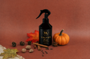 A dark spray bottle labeled 'VELVET home' stands on a warm rust-brown background with autumn props including a small pumpkin, cinnamon sticks, pinecones, nuts, leaves, and a red maple leaf.