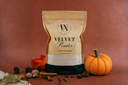A stand-up pouch of Velvet Powder luxury freshener by The Velvet Noble, styled on a warm brown background with a small orange pumpkin, cinnamon sticks, cloves, and autumn leaves.