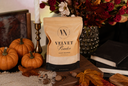 A stand-up pouch of Velvet Powder luxury freshener by The Velvet Noble, styled on a wooden surface with pumpkins, autumn leaves, books, and a candle holder in a warm fall setting.