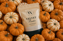 A stand-up pouch of Velvet Powder luxury freshener centered among many small pumpkins and gourds. The pouch is cream with a black base and printed logo/text.