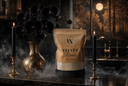 A stand-up pouch labeled 'VELVET Powder' by The Velvet Noble stands on a dark countertop in a moody interior scene with black candles, a gold vase of dark flowers, and a warm-toned background.