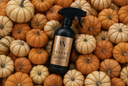 A black spray bottle labeled 'VN. Velvet Sparkle' sits centered on a dense arrangement of small orange and cream pumpkins.