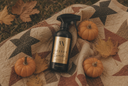 A dark spray bottle labeled 'Velvet Sparkle' sits on a quilted star blanket with pumpkins and autumn leaves around it.