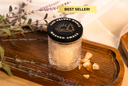 Candle in a textured jar with a black lid on a wooden tray, surrounded by lavender and amber pieces.