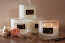 Three decorative candles with a VN brand label on a wooden surface.