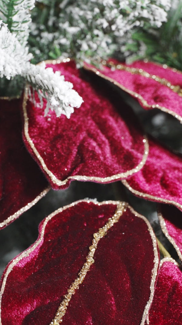 A downward panning video of red velvet magnolia leaves with gold trim in a flocked christmas tree